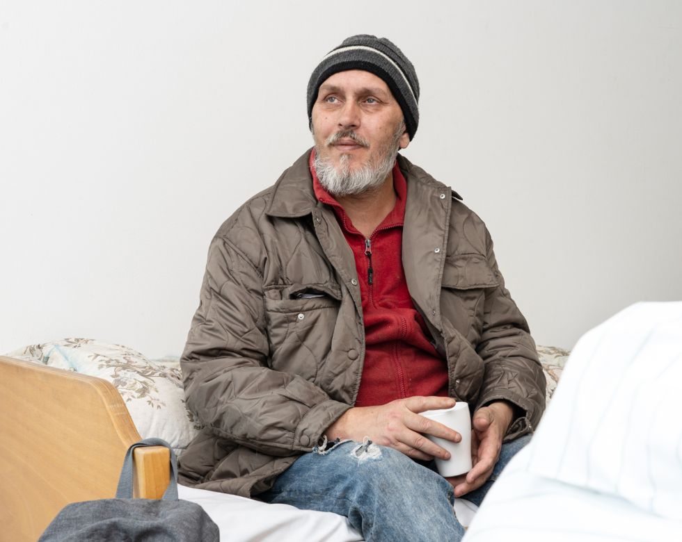 Ein Mann sitzt mit einer Kaffeetasse auf einem Bett.
