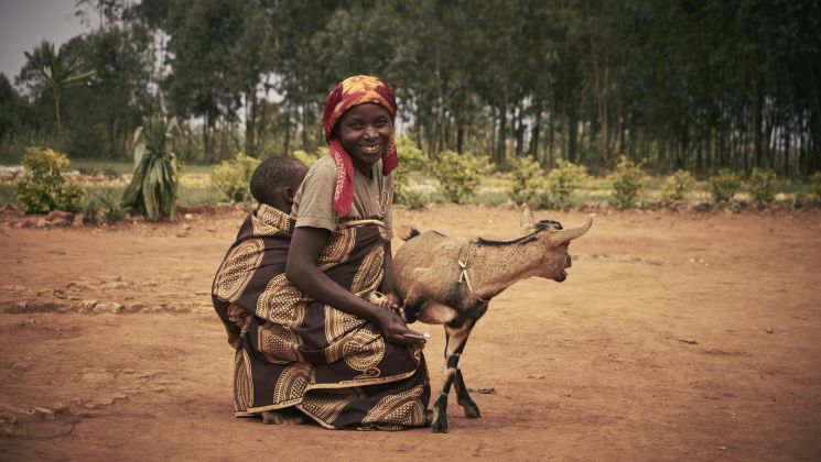 Eine Frau in afrikanischen Gewändern mit Baby und einer Ziege.