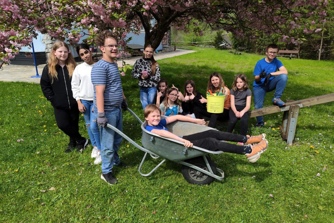Gruppenfoto von Schüler*innen im Garten. Ein Schüler sitzt in einer Scheibtruhe.