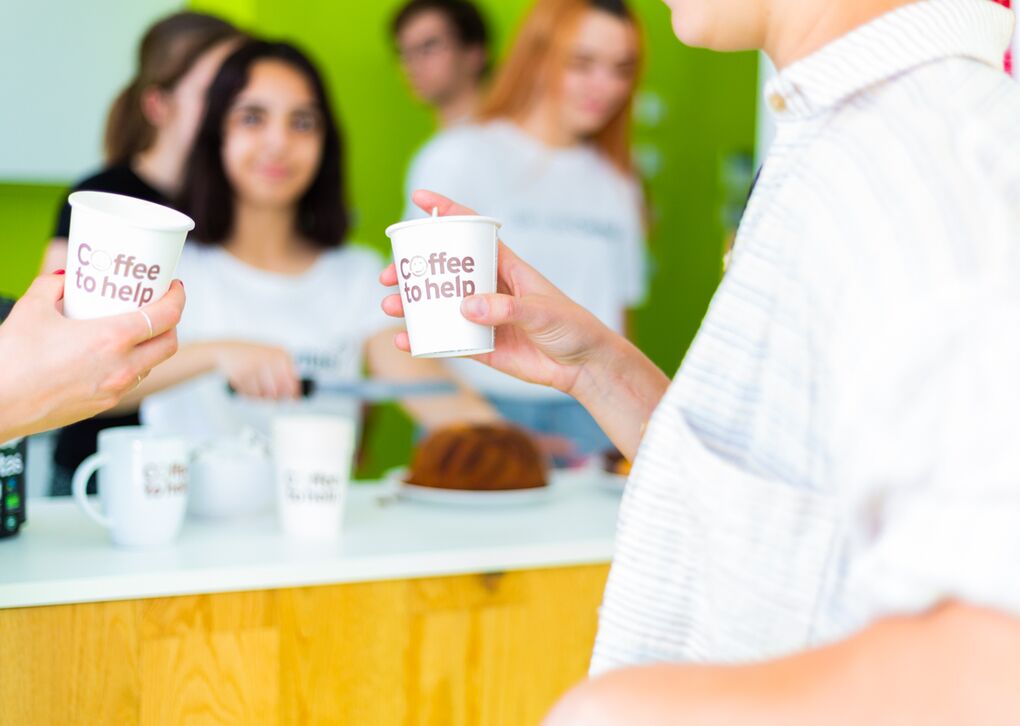 Zwei Personen stoßen mit einem Coffee to help-Becher an.