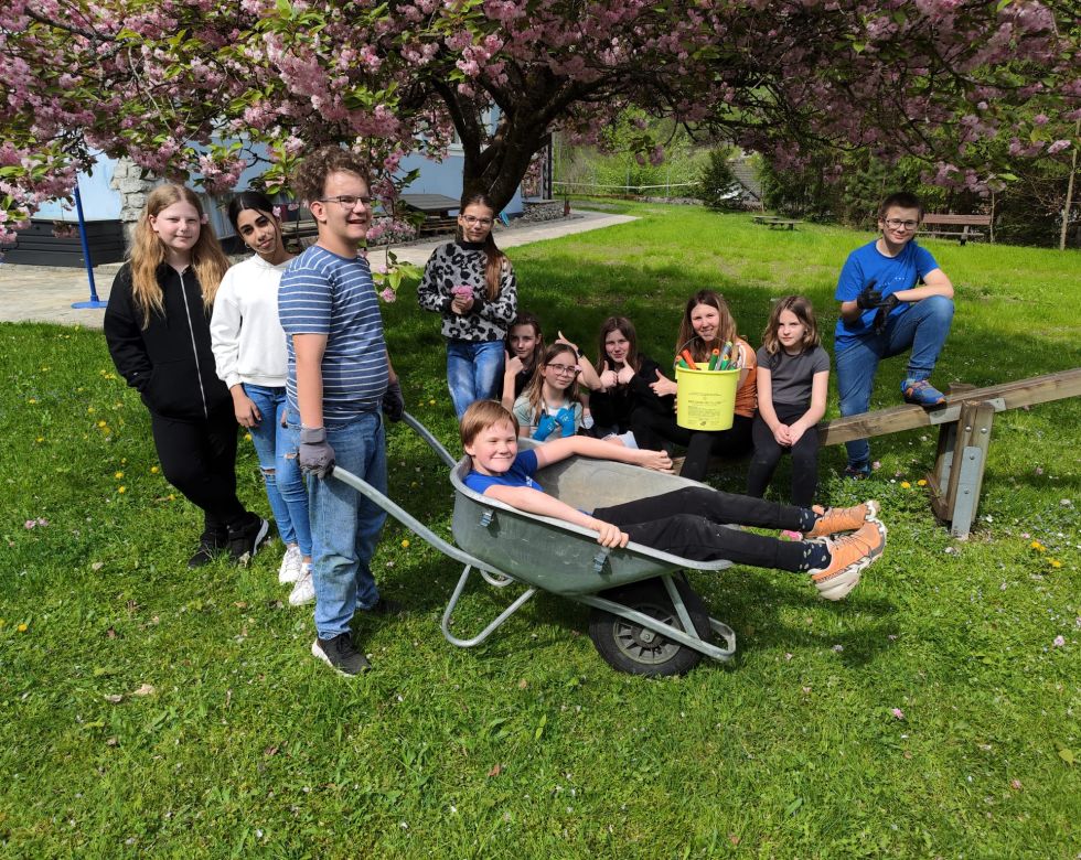 Gruppenfoto von Schüler*innen im Garten. Ein Schüler sitzt in einer Scheibtruhe.