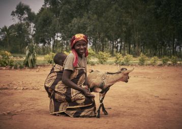 Eine Frau in afrikanischen Gewändern mit Baby und einer Ziege.