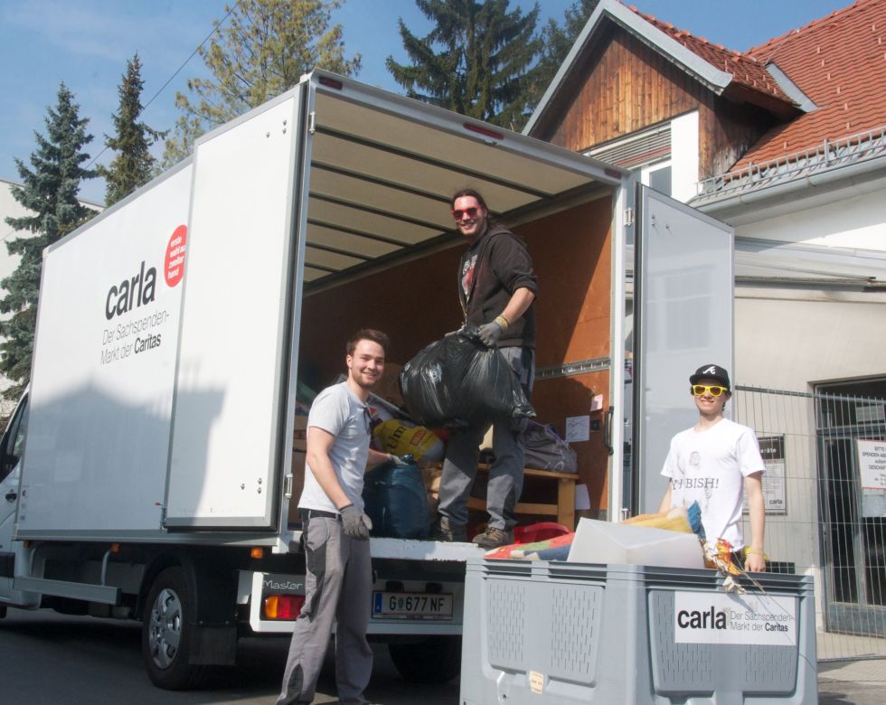 Drei junge Männer beim Beladen eines weißen Transportwagens mit dem Schriftzug "carla".
