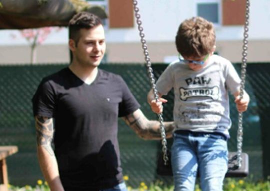 Ein Mann unterstützt einen Jungen beim Schaukeln in einem Park an einem sonnigen Tag