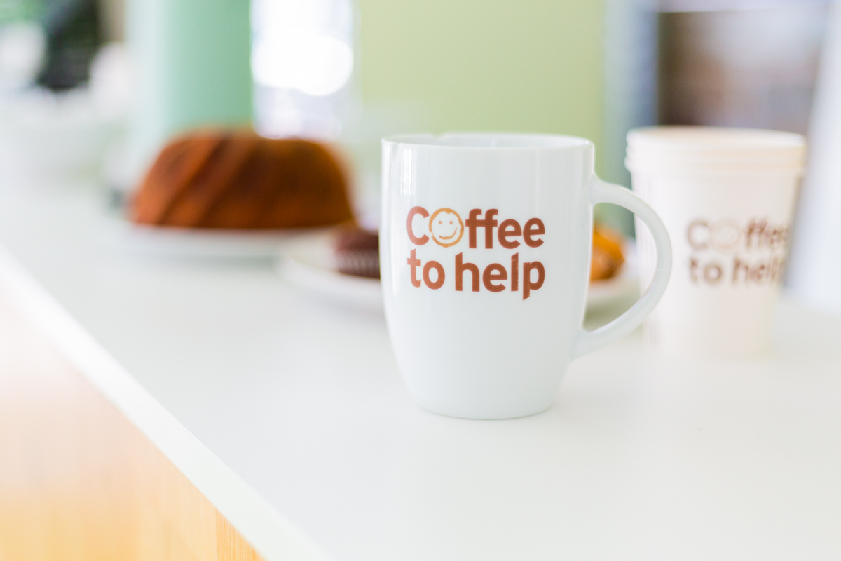 Coffee to help-Kaffeetasse mit Kuchen im Hintergrund.