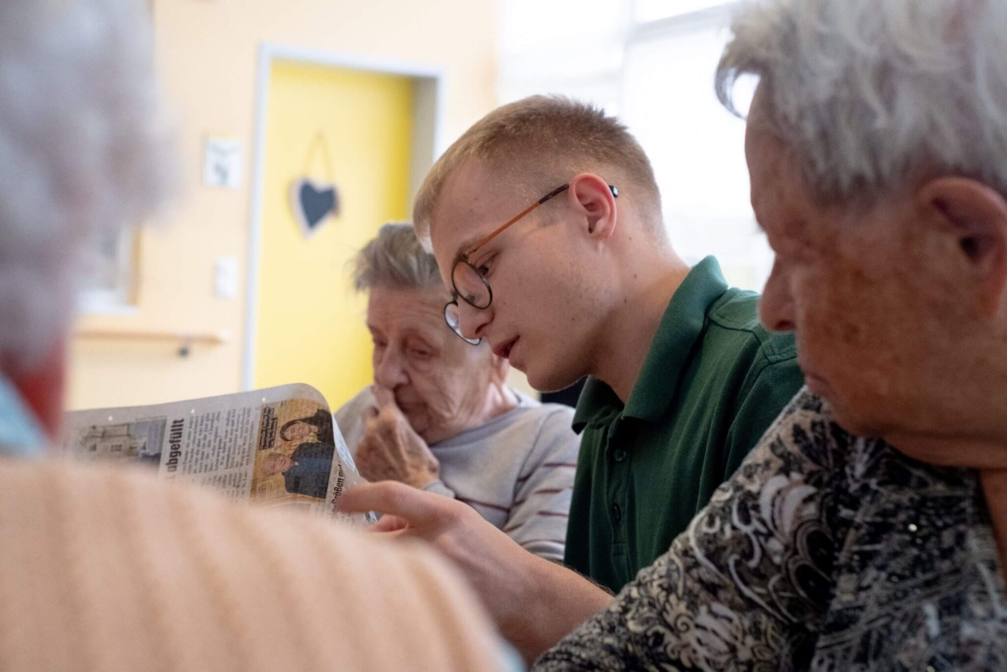 Ein Zivildiener liest mit älteren Personen Zeitung.