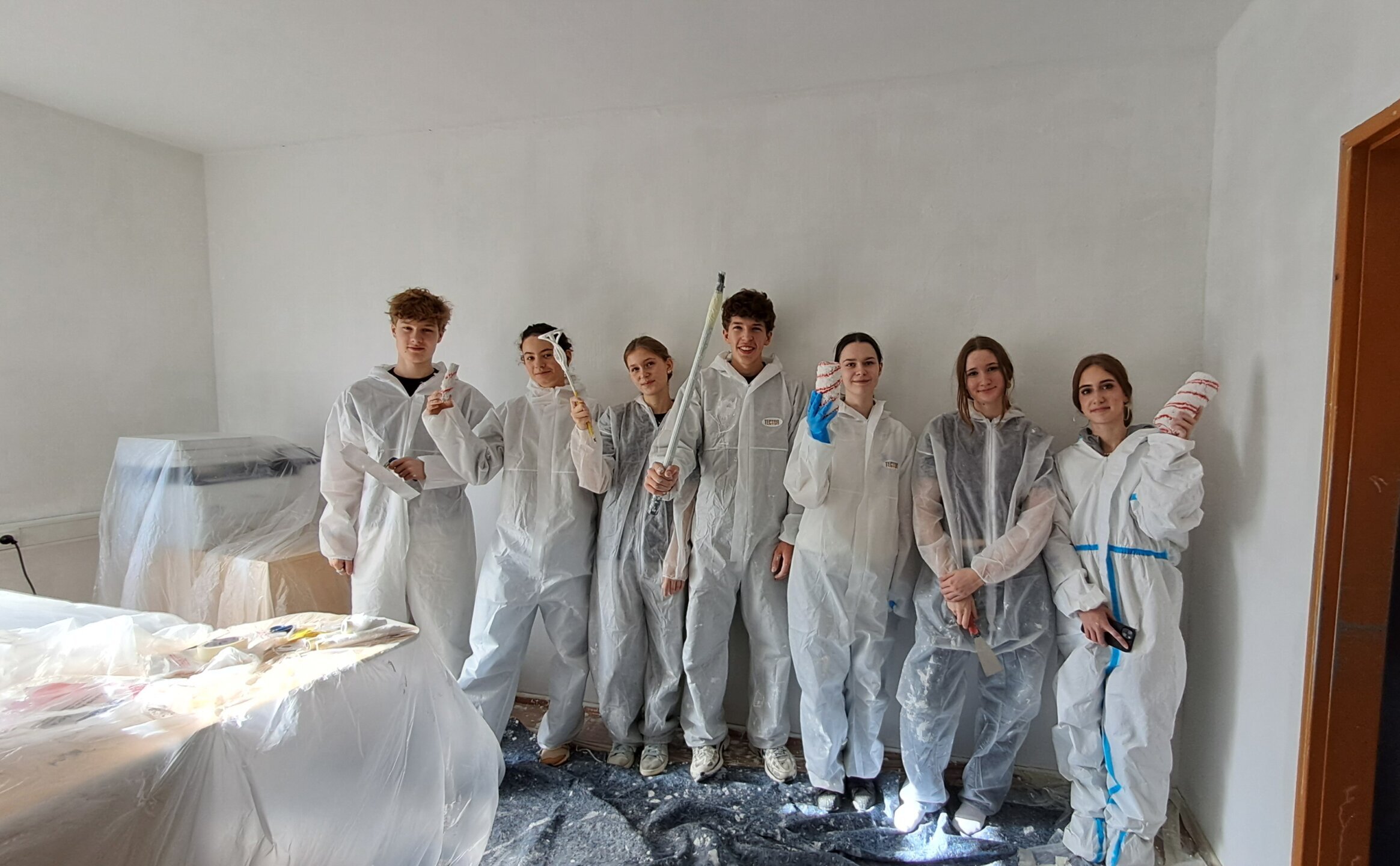 Schüler*innen in weißen Malergewändern und mit Malwerkzeug in der Hand posieren für die Kamera.