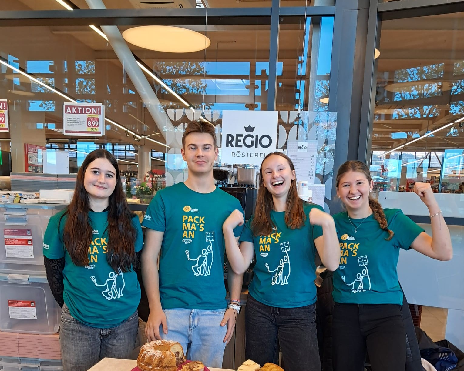 Jugendliche verkaufen Kuchen. Alle tragen T-Shirts mit dem Aufdruck 
