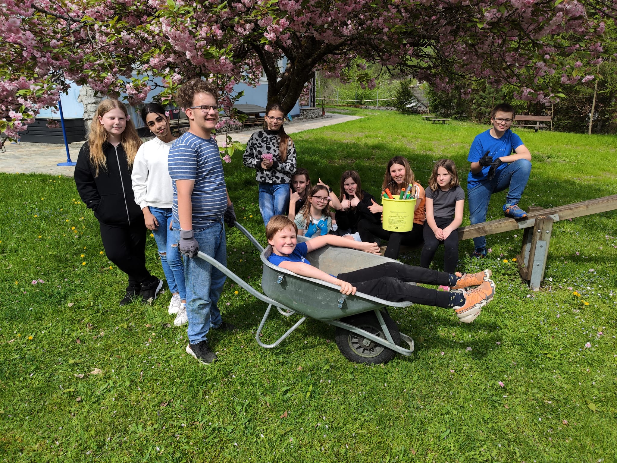 Gruppenfoto von Schüler*innen im Garten. Ein Schüler sitzt in einer Scheibtruhe.